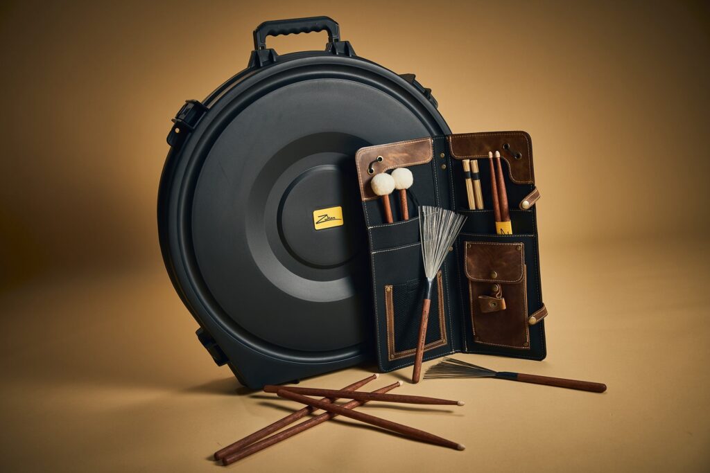 Black Zultan cymbal case with a brown leather drumstick holder and several drumsticks scattered on the floor.