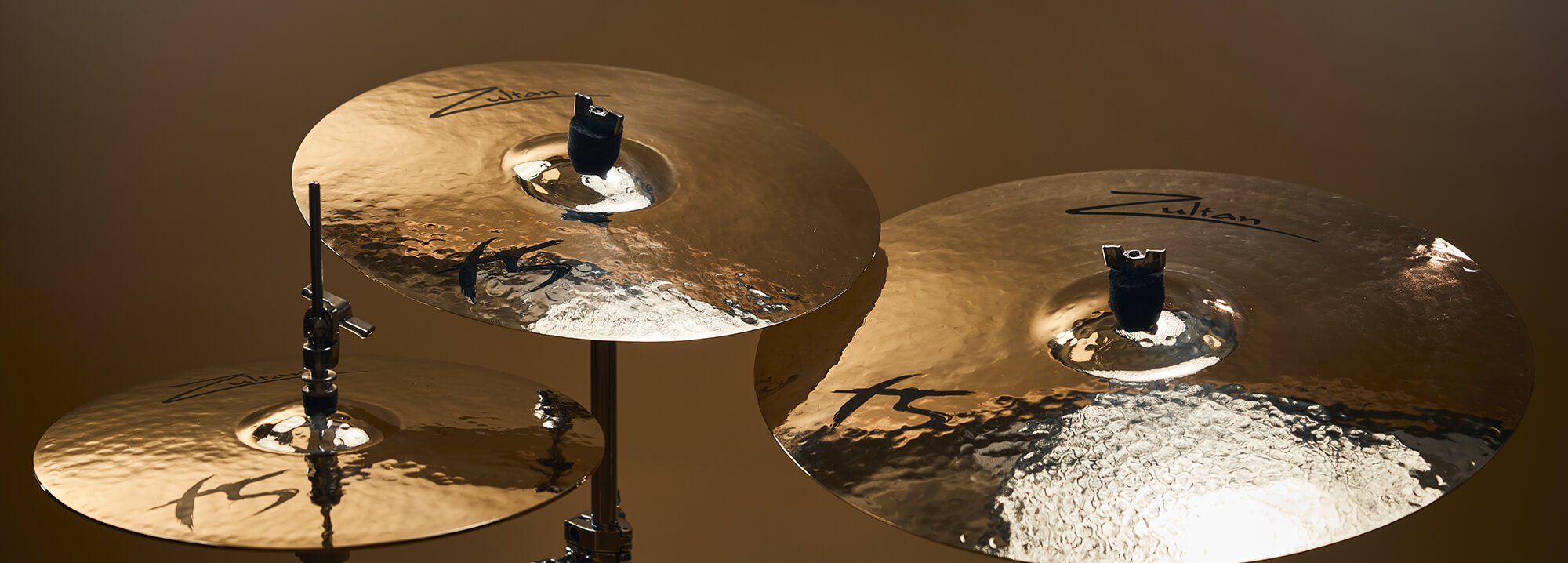 Three Zultan F5 series cymbals of varying sizes, mounted on stands against a warm background.