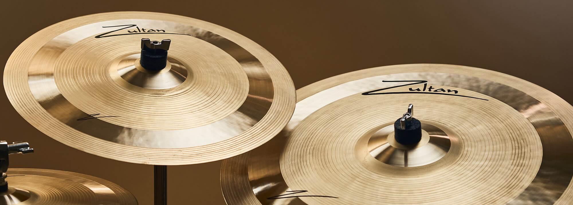 Three Zultan Z series cymbals of varying sizes, mounted on stands against a warm background.