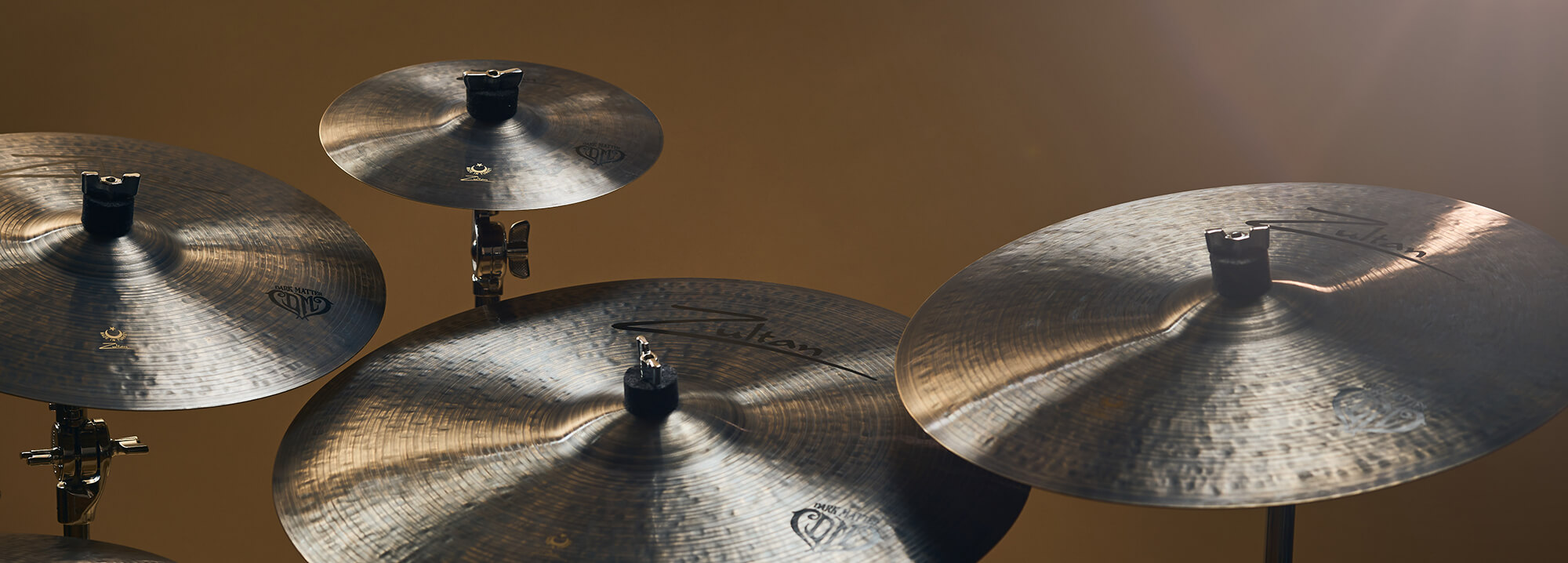 Four Zultan Dark Matter cymbals on stands, angled towards the viewer against a warm-toned background.