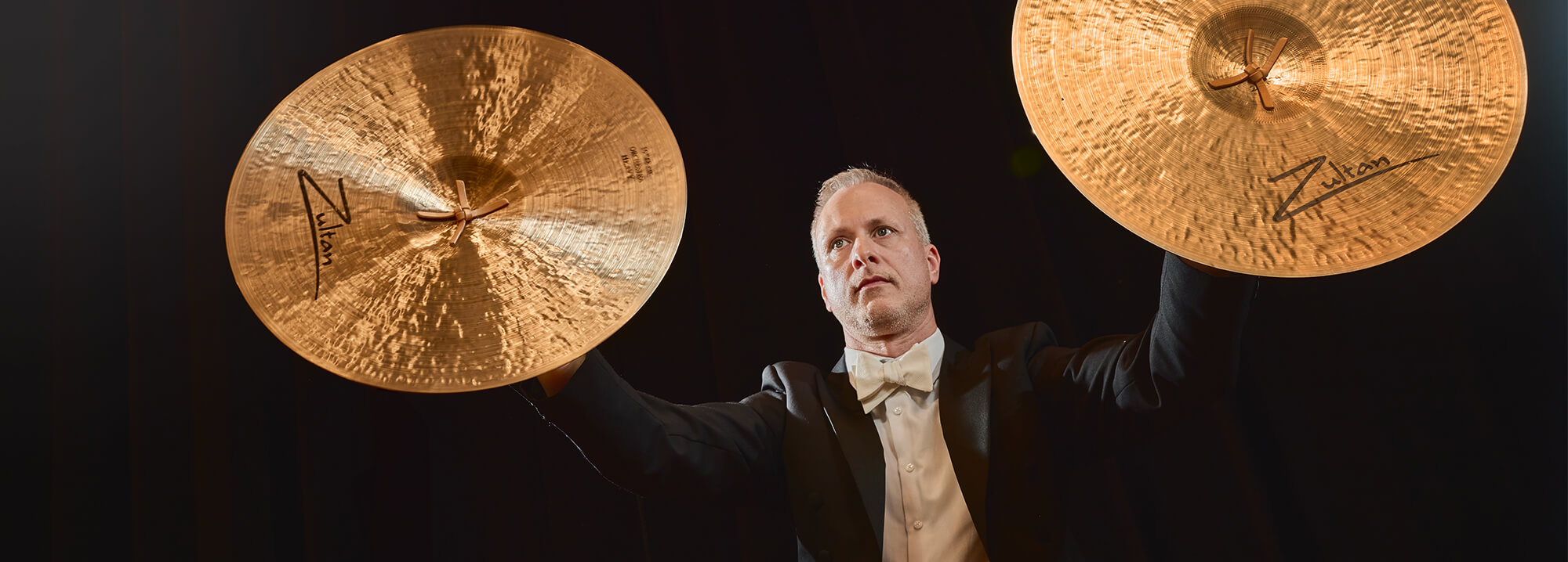 A man holding two Zultan Orchestra series cymbals up high