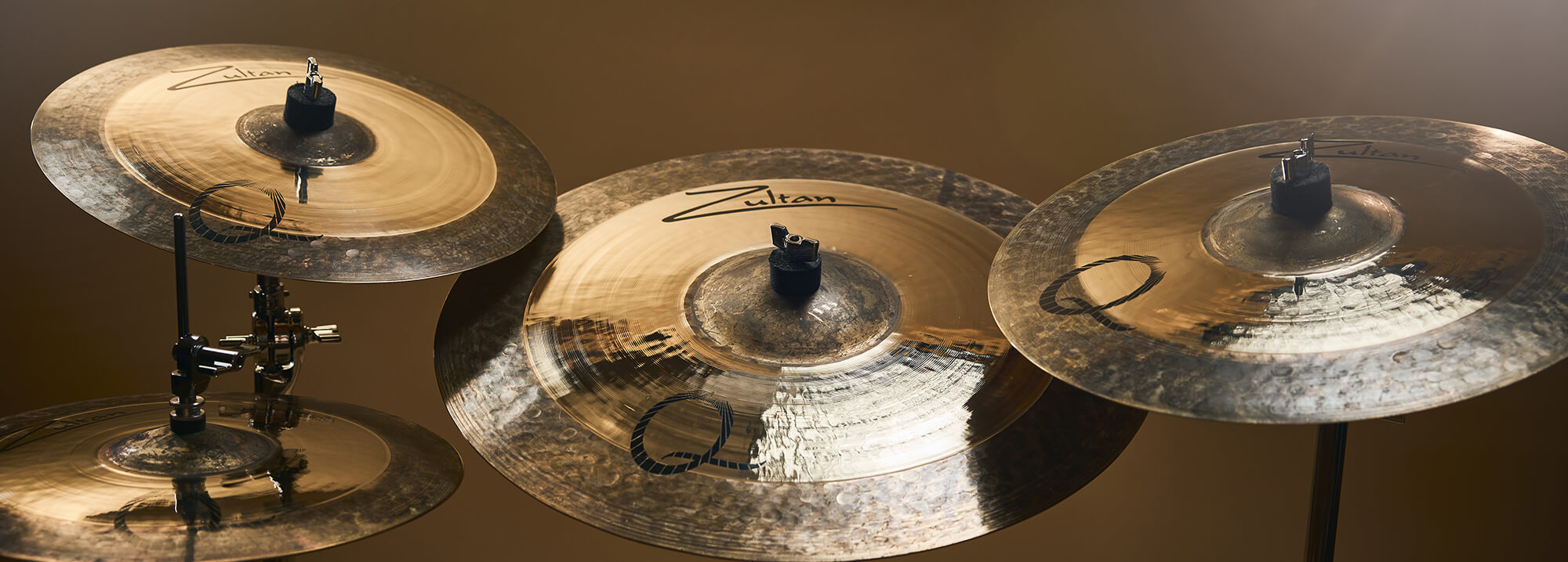 Four Zultan Q series cymbals of varying sizes, mounted on stands against a warm background.
