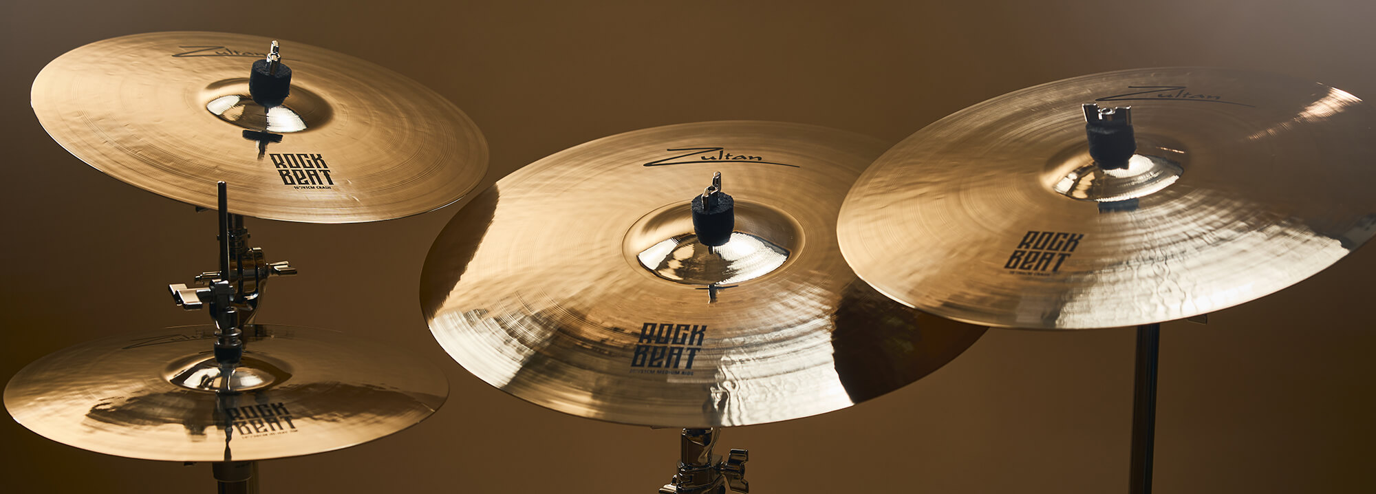 Four Zultan Rock Beat series cymbals of varying sizes, mounted on stands against a warm background.
